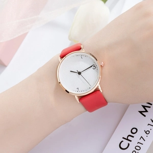 Close-up of minimalist women's watch with red leather strap and gold case on wrist