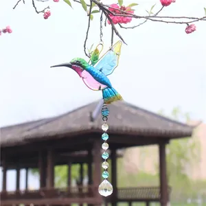 Detail of hummingbird crystal pendant hanging on pink floral branches in a garden