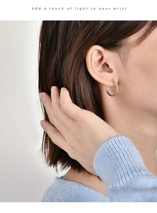 Detailed view of a woman wearing gold-plated spiral twisted hoop earrings with a chic finish