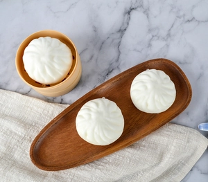 Realistic white bun squishy toy in yellow steamer on a minimalist wooden tray
