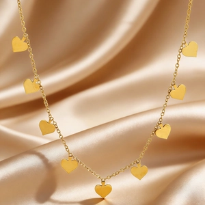 Close-up of golden stainless steel necklace with small heart charms on silk background