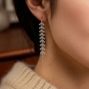 Elegant gold-tone leaf fringe earrings with baguette-cut zircons worn by a model
