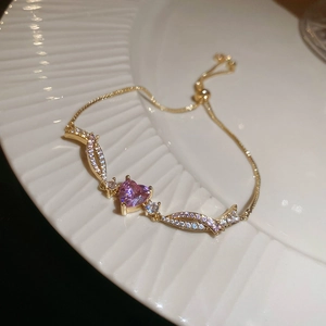 Close-up of adjustable gold heart bracelet with purple zircon on white ceramic plate
