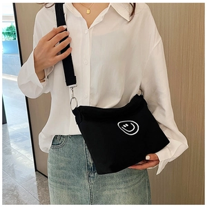 Detail of black canvas crossbody bag featuring a white smiley face and adjustable wide strap