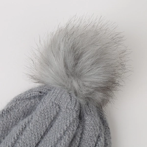 Close-up of grey knit beanie with cable pattern and fluffy faux fur pompom detail
