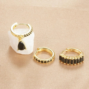 Detail of three-piece gold-plated earring set featuring black stones on silk background