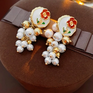 Détail de boucles d'oreilles vintage en émail fleuri avec perles blanches et accents dorés