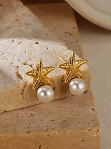 Macro detail of golden starfish earrings with white pearls on natural stone background