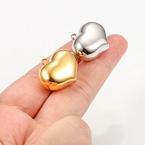 Polished 3D hollow heart pendants in gold and silver finish shown for scale on finger