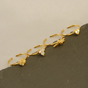 Golden 4-piece ring set with rose, bow, and heart designs on a grey rock background
