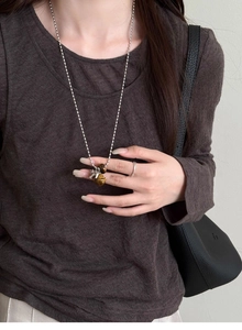 Detail view of tiger eye bell horse pendant on long silver chain worn by a model