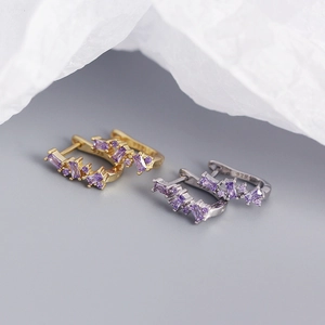 Macro shot of U-shaped S925 silver earrings with purple zircons in gold and silver finish