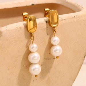 Boucles d'oreilles asymétriques en perles dorées à l'or 18 carats sur un pot en céramique