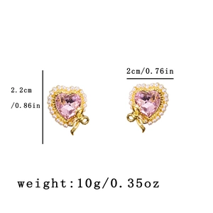 Detail view of heart-shaped pink crystal earrings with pearls and a gold bow, 2.2x2cm size