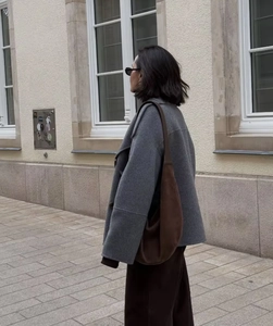 Outdoor shot of a grey wool coat paired with a large brown suede shoulder bag