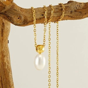 Close-up of elegant oval pearl and faceted gold bead pendant on a branch