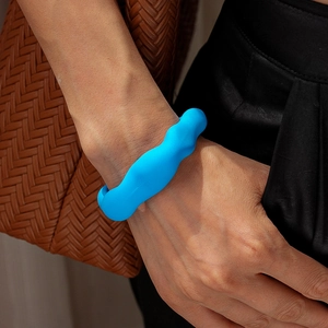 Nahaufnahme eines blauen Acrylarmreifs mit Wellenstruktur am Handgelenk des Models