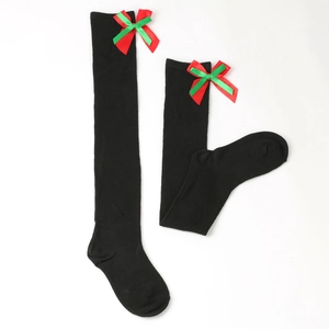 Detail of black over-the-knee Christmas socks with red and green ribbon bow accents