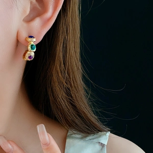 Close-up of vintage golden C-shaped earring with blue green and purple gemstones