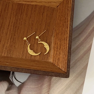 Macro detail of 925 silver moon face stud earrings in gold finish on wood tray
