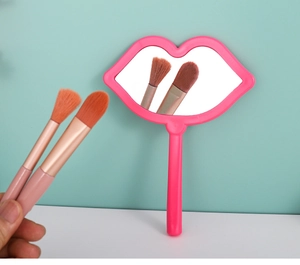 Pink lip-shaped hand mirror and two matching makeup brushes on a clean aesthetic surface