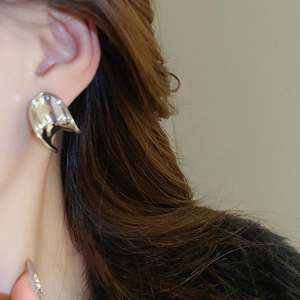 Close-up of liquid metal style C-shaped earring with irregular silver finish on ear