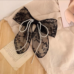 Close-up of black lace bow hair clip with white pearl bead accents on a beige fabric