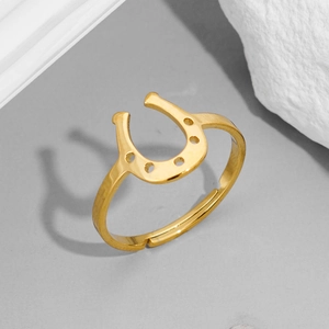 Gros plan d'une bague fer à cheval dorée en U sur fond en pierre grise minimaliste