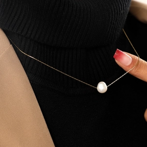 Minimalist stainless steel necklace with white pearl pendant worn on black turtleneck