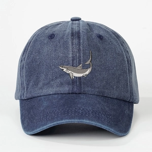 Detailed embroidery of a great white shark on a washed blue denim baseball cap surface