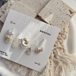 Macro detail of 5D embossed nail charms featuring pearls, bows and rhinestones on cream tips