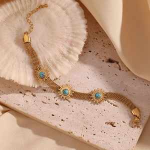 Macro detail of 18K gold braided bracelet with turquoise sun charms on coral background