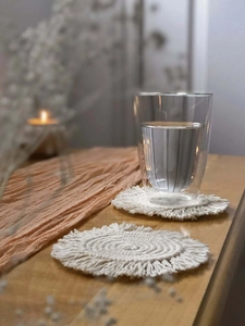 Detail of round cotton woven coasters with fringe tassels on a wooden table with glass
