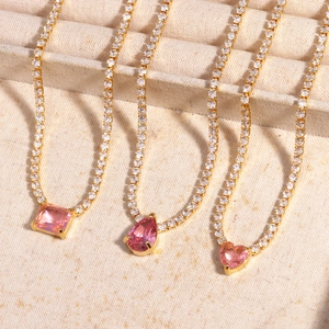 Detailed view of three gold tennis chains with pink heart, drop, and rectangle pendants