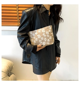 Detailed view of beige embroidered floral clutch held against a black leather shirt