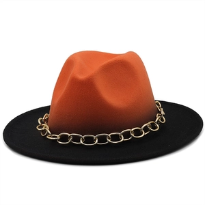 Detail of fedora hat featuring orange crown, black brim and chunky gold metal chain