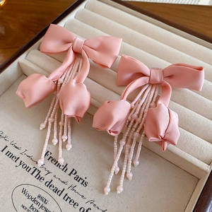 Detail view of pink fabric bow earrings with delicate beaded tassels on a wooden tray