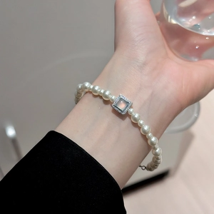Detail of elegant pearl bracelet with a square moonstone charm on a model's wrist