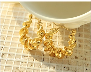 Detail of gold twisted croissant hoop earrings with a secure clasp on a marble stone surface