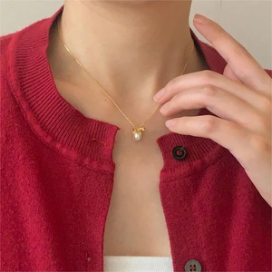 Macro shot of pearl bow necklace on model wearing a vibrant red knitted sweater