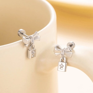 Silver bow stud earrings with cross lock pendant on minimalist ceramic surface