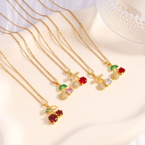 Elegant gold cherry pendant necklaces with colorful zircon stones on white silk background