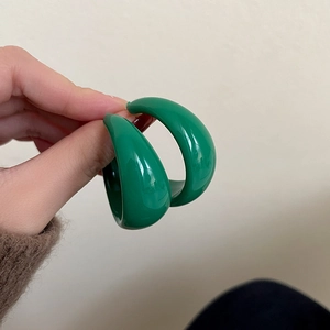 Minimalist green C-shaped hoop earrings in shiny resin held in hand against plain wall