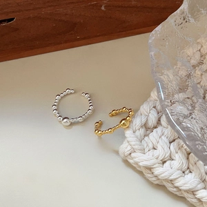 Close-up of minimalist beaded open rings in gold and silver finish on textured decor