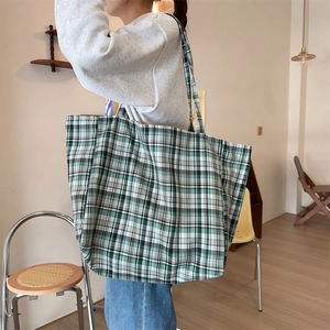 Detail shot of a large plaid canvas tote bag worn over the shoulder in a lifestyle setting