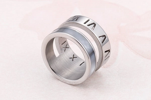 Macro shot of silver stainless steel ring with engraved Roman numerals on pink background