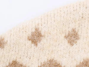Vista macro del tessuto a maglia crema con motivo a rombi marroni e consistenza morbida