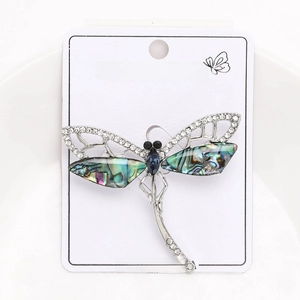 Detailed macro view of silver dragonfly brooch with crystals and abalone shell in a bowl