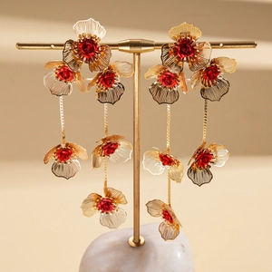 Détail de boucles d'oreilles à pampilles avec pétales dorés et cœurs de fleurs rouges