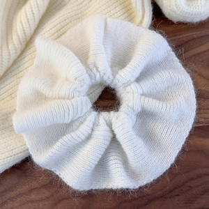Close-up of a white knit scrunchie with soft ruffled wool texture on a wooden surface